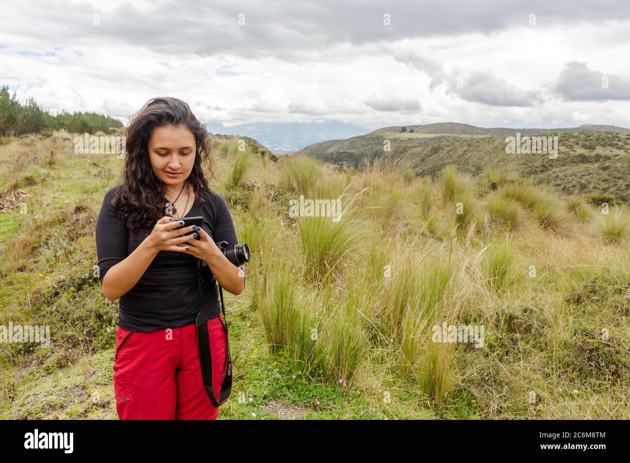 Donna che controlla il suo cellulare su una montagna con una macchina fotografica sul braccio Foto Stock