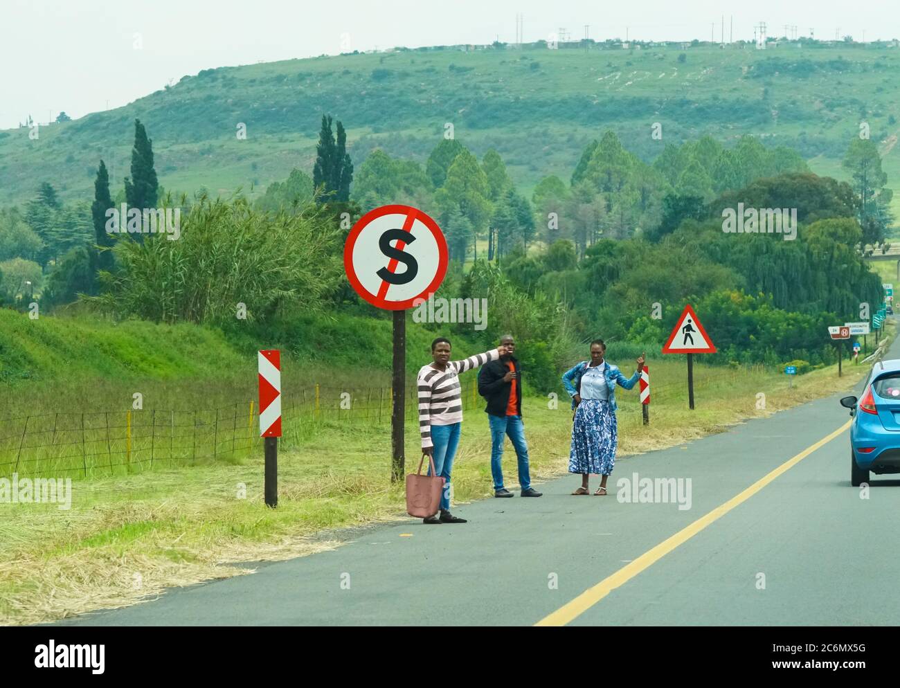 Gli escursionisti africani che si trovano sul lato dell'autostrada sotto un cartello che indica che non si fermano cercando di far salire a Johannesburg, in Sudafrica Foto Stock