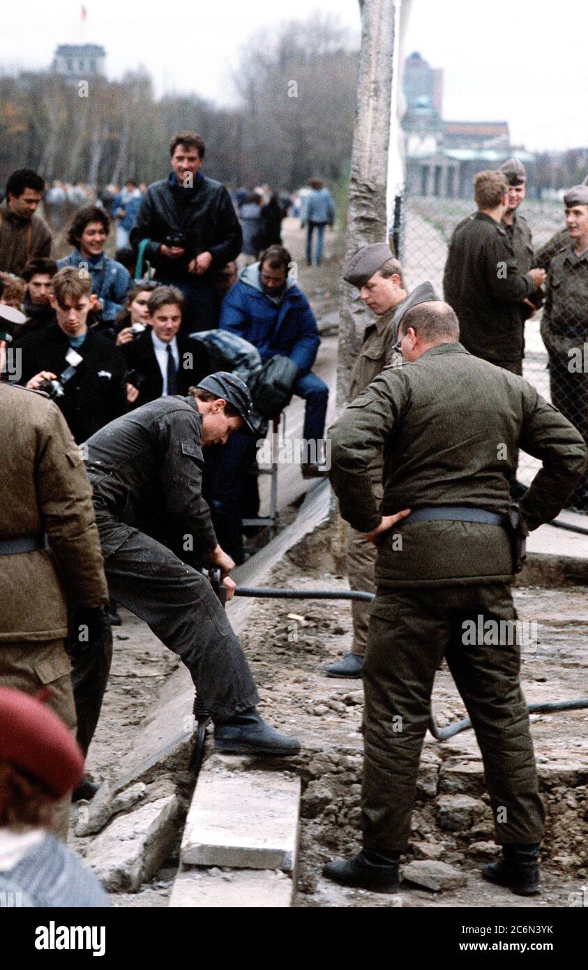 Oriente polizia tedesca e a ovest di cittadini tedeschi guardare come un operaio smantella una sezione del muro di Berlino a Potsdamer Platz. Foto Stock