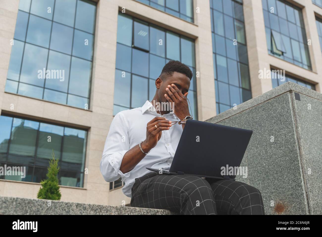 Sensazione di sfinito. Un giovane africano nero, frustrato, che tiene gli occhi chiusi e si stanca di lavorare extra sul notebook Foto Stock