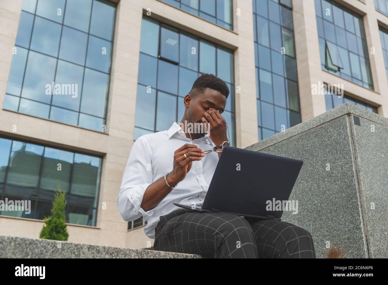 Sensazione di sfinito. Un giovane africano nero, frustrato, che tiene gli occhi chiusi e si stanca di lavorare extra sul notebook Foto Stock