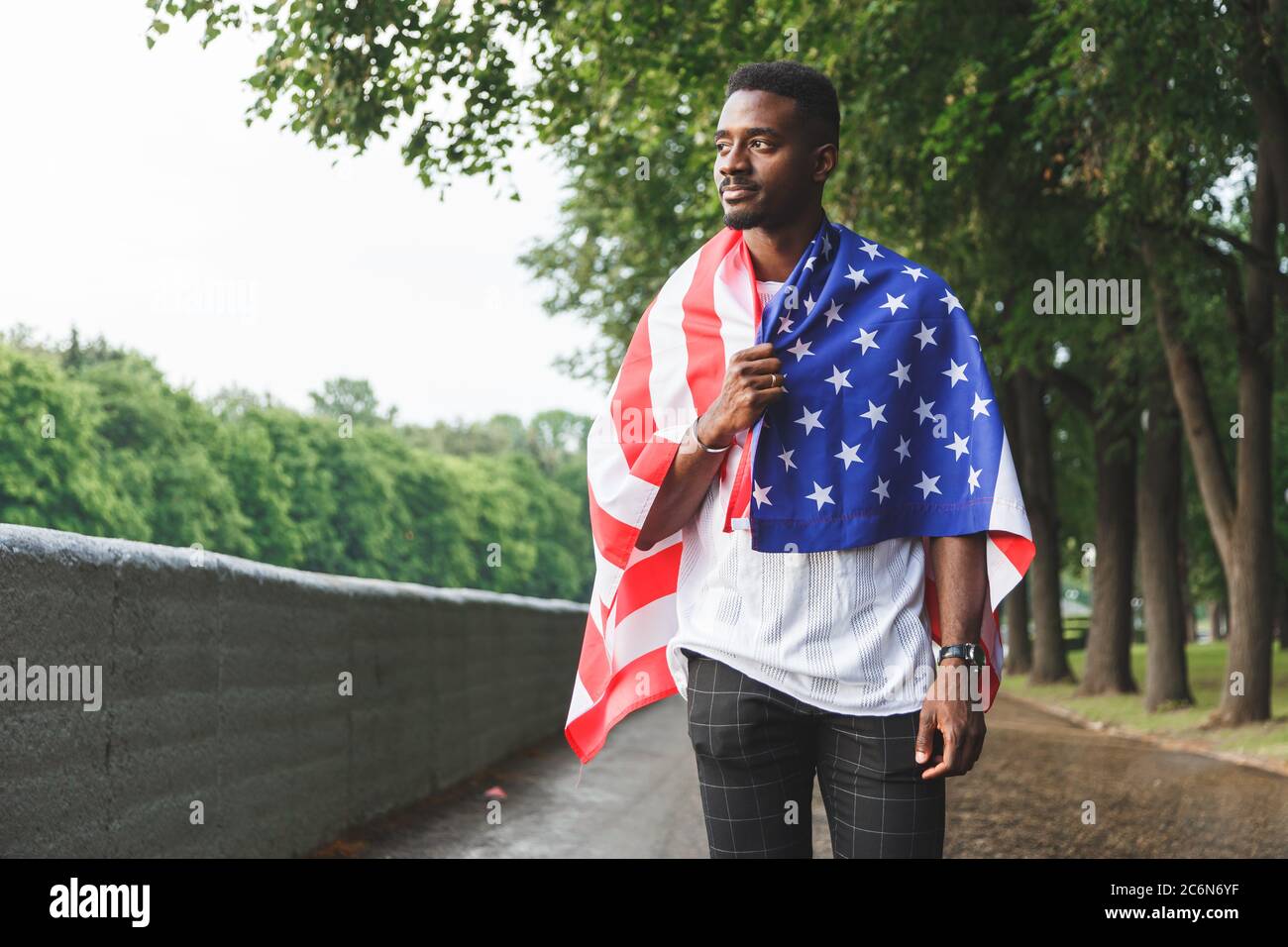 Afro americano uomo con bandiera degli Stati Uniti sulle spalle in piedi all'aperto. Giorno estate Foto Stock