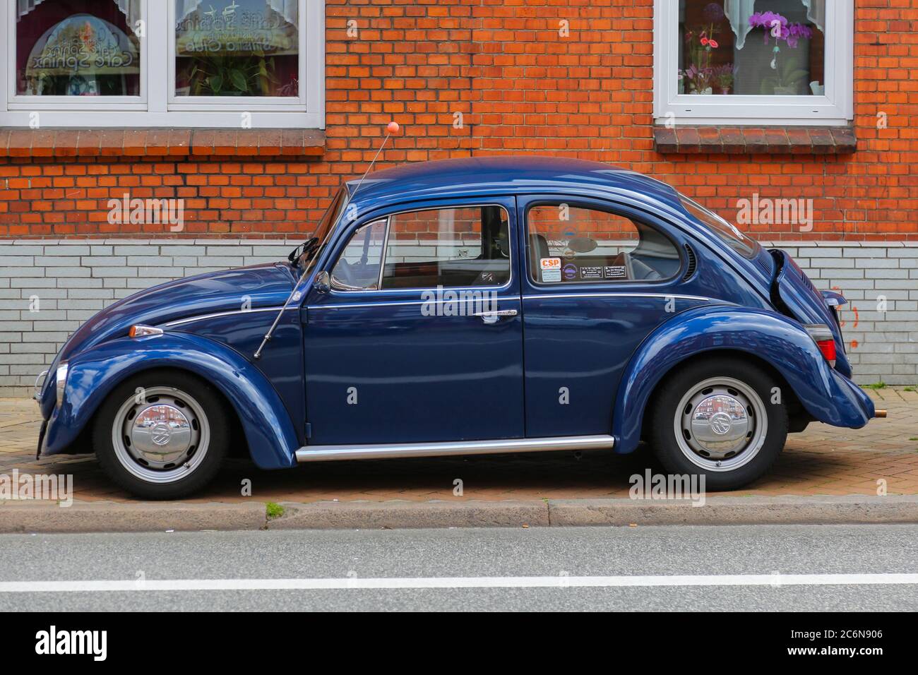 Un classico Maggiolino Volkswagen blu parcheggiato in una tranquilla via Kiel, incorniciato da edifici in mattoni rossi e grigi con finestre bianche e decorazioni floreali. Foto Stock