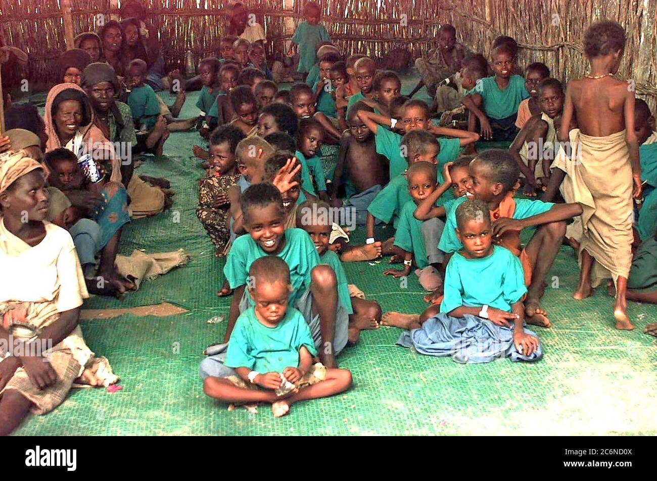 1992 - dritto girato all'interno di Bamboo Hut a diversi bambini Somali seduti in fila su di un tappeto verde. Quasi tutti i bambini sono indossando le t-shirt verdi. Alcuni vecchi donne somale sono visto seduto in una fila a sinistra del telaio. Foto Stock
