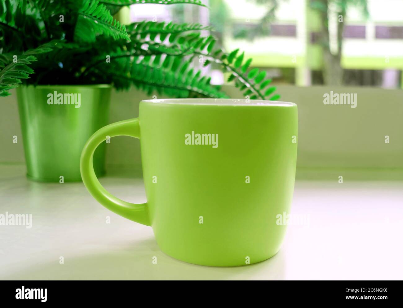Tazza di caffè in stile pop art di colore verde sul tavolo con una felce in vaso sullo sfondo Foto Stock