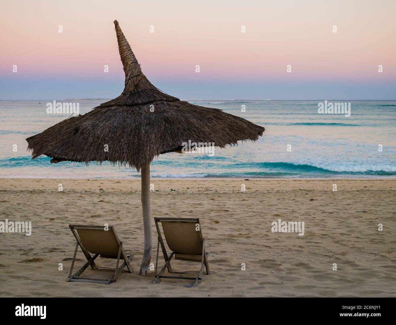 Incredibile alba con un tradizionale ombrellone in paglia e due sdraio che si affacciano sulla tranquilla costa dell'Oceano Indiano, Anakao, Madagascar Foto Stock