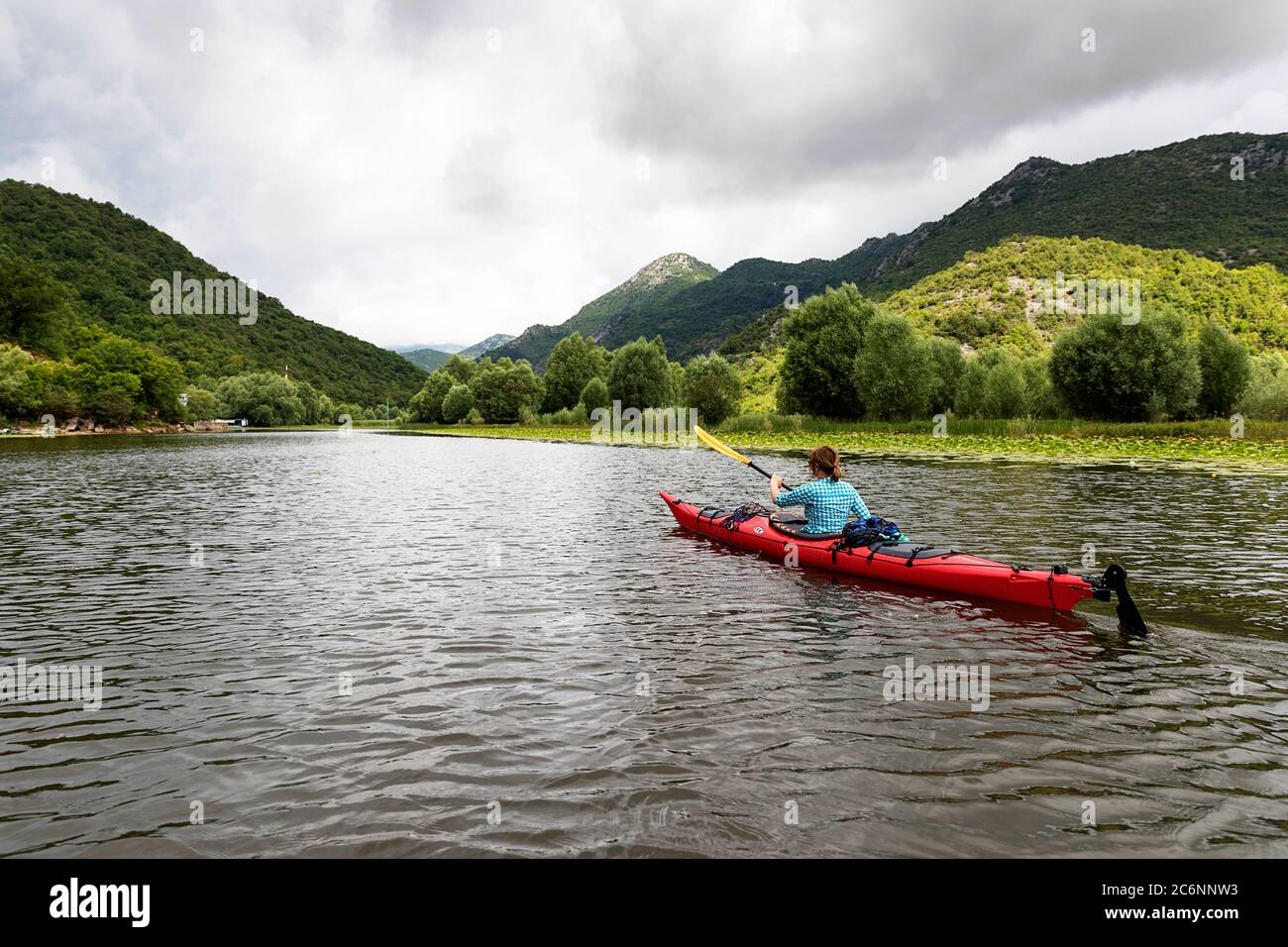 Donna in kayak rosso che addlata tra le ninfee sul lago Skadar, Montenegro Foto Stock