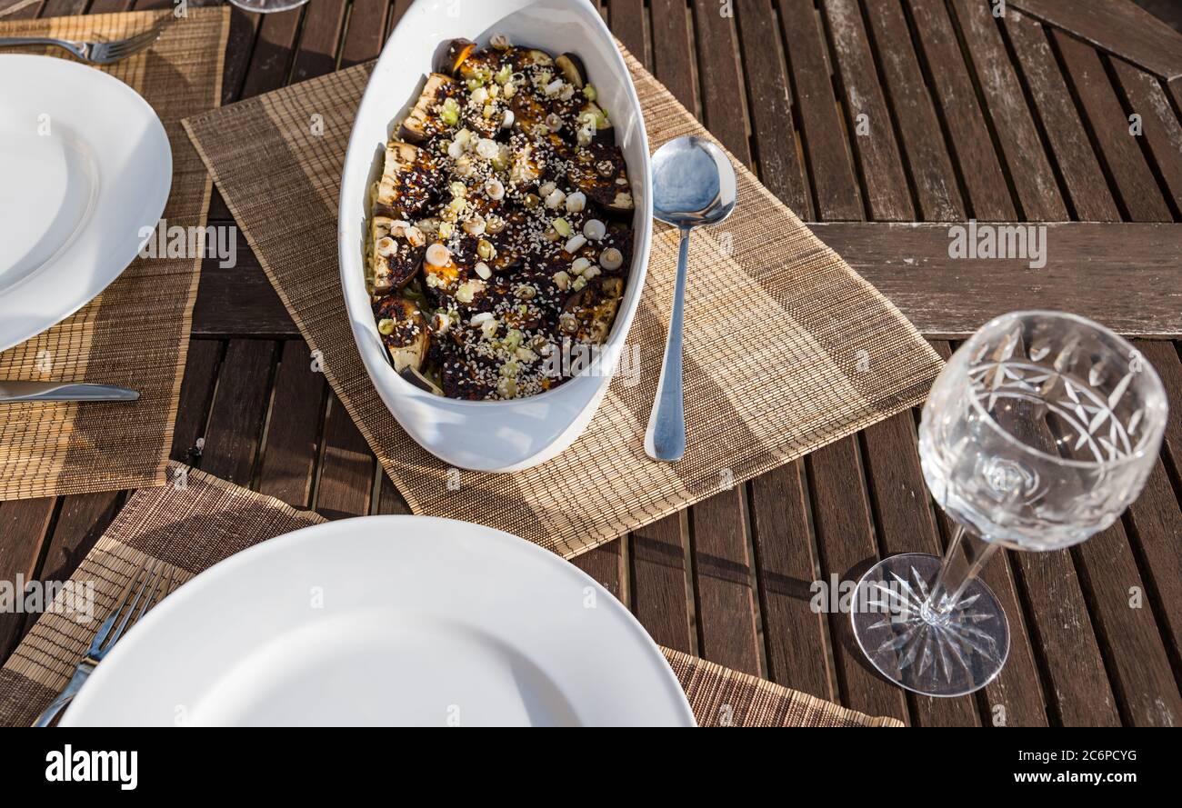 Piatto di melanzane speziate coreane servito sul tavolo da patio all'aperto sotto il sole con bicchiere di vino di cristallo, Scozia, UK Foto Stock