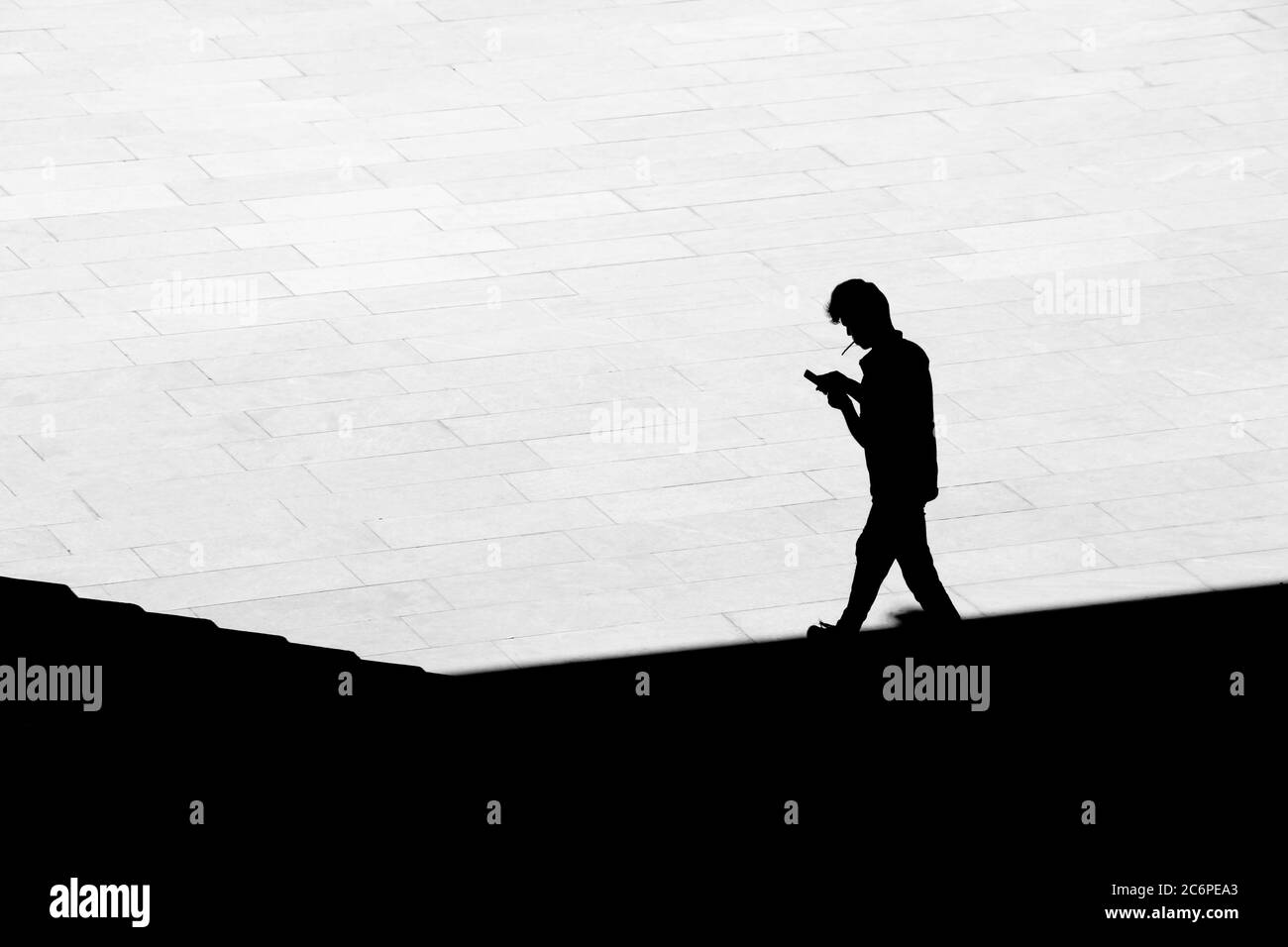 Silhouette di un uomo che fuma una sigaretta mentre cammina dall'ombra sulla piazza della città, vista posteriore ad angolo alto Foto Stock
