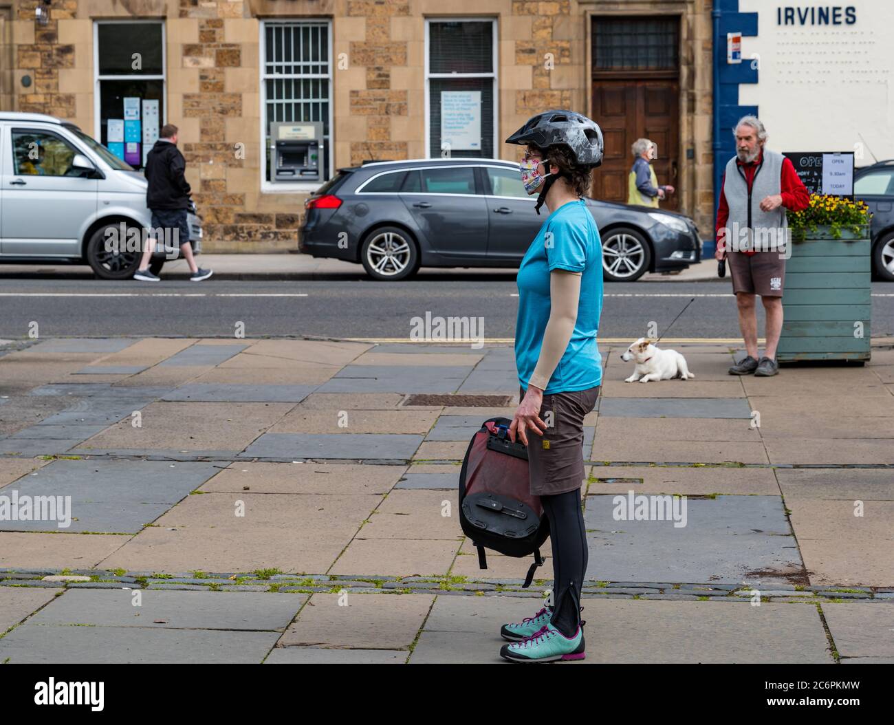 Donna ciclista femminile che indossa maschera facciale e casco da bicicletta in coda per il mercato agricolo durante la pandemia di Covid-19, Haddington, East Lothian, Scozia, Regno Unito Foto Stock