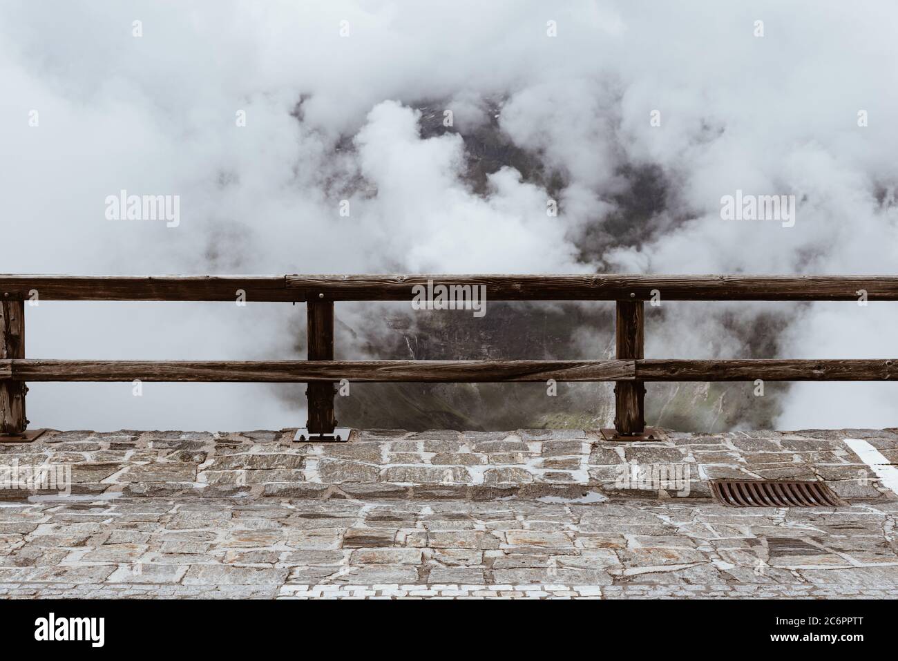 Nuvole bianche sotto la montagna con una recinzione in legno su un marciapiede lastricato Foto Stock