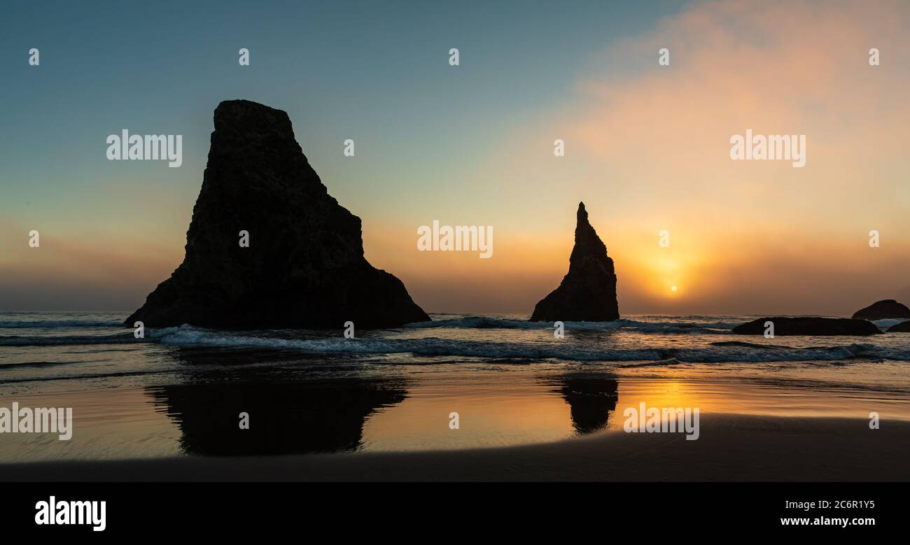 Il colorato tramonto illumina il cielo dietro le pile di mare sulla spiaggia di Bandon, in Oregon Foto Stock