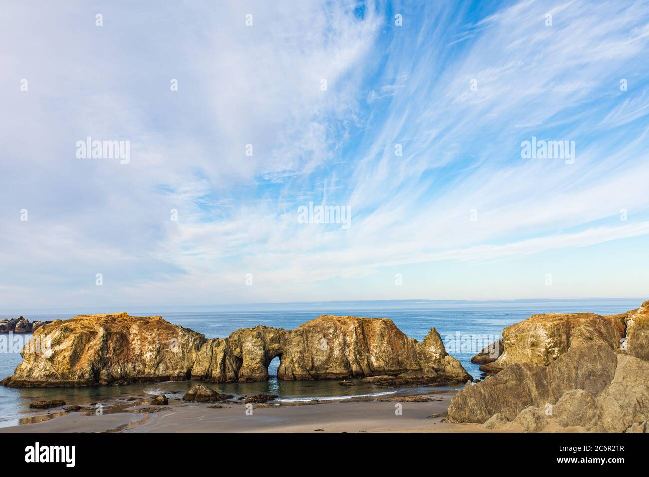Guardando verso il basso verso una spiaggia sabbiosa con un grande catasta di mare appena fuori dalla costa e un cielo con nuvole uniche Foto Stock