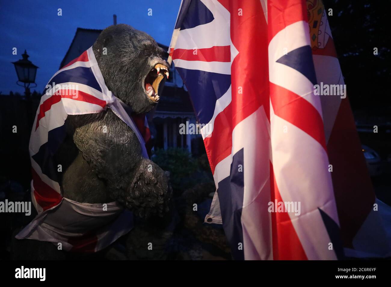 Un gorilla di plastica è avvolto nella bandiera dell'Unione da un falò sulla Shankill Road di Belfast, poiché i falò erano stati accesi a mezzanotte, Come parte di una tradizione lealista per celebrare l'anniversario della vittoria del re protestante Guglielmo sul re cattolico Giacomo nella battaglia del Boyne nel 1690. Foto Stock