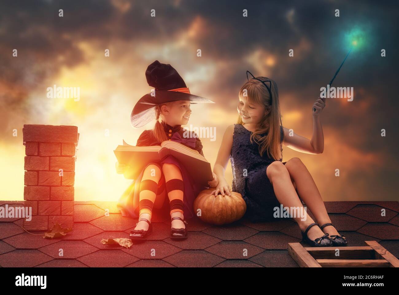 Due sorelle felici su Halloween. Bambini divertenti in costumi di carnevale  seduti sul tetto. Bambini allegri con zucca, bacchetta magica e libro di  incantesimi Foto stock - Alamy