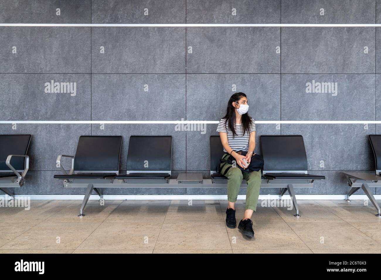 Giovane donna con maschera di protezione è seduta in una sala d'attesa e guardando intorno all'aeroporto. Interruzione del virus corona. Foto di alta qualità Foto Stock