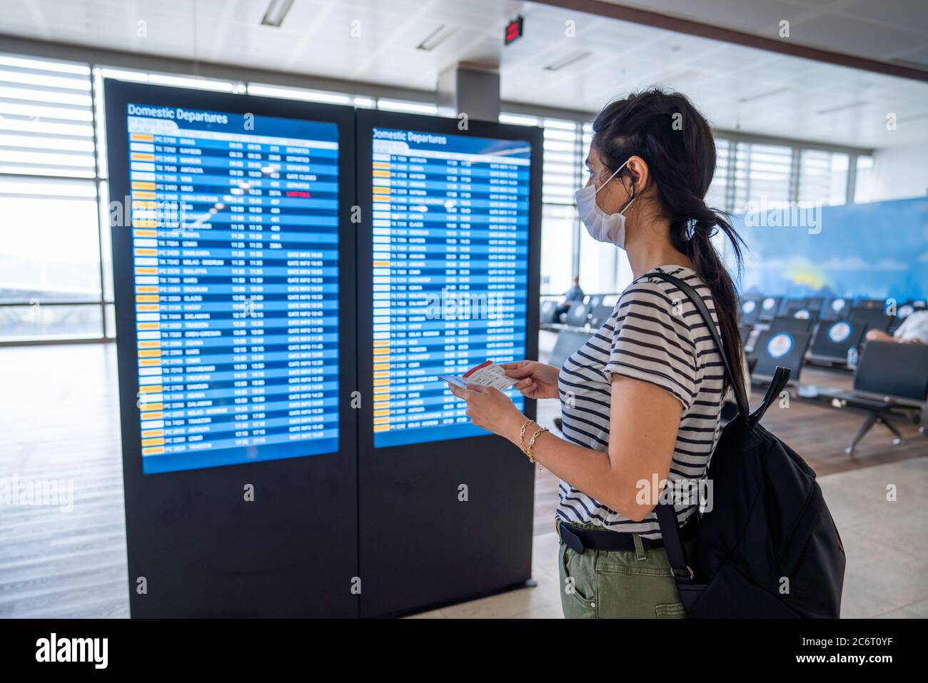 Giovane donna in protezione antivirus maschera di protezione guardando il bordo di informazioni in aeroporto. Interruzione del virus corona. Foto di alta qualità Foto Stock