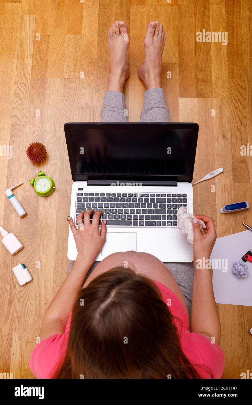 Donna incinta che lavora da casa. Freelance che utilizza un notebook. Posto di lavoro sul pavimento con farmaci. Concetto di business, carriera, educazione domestica Foto Stock