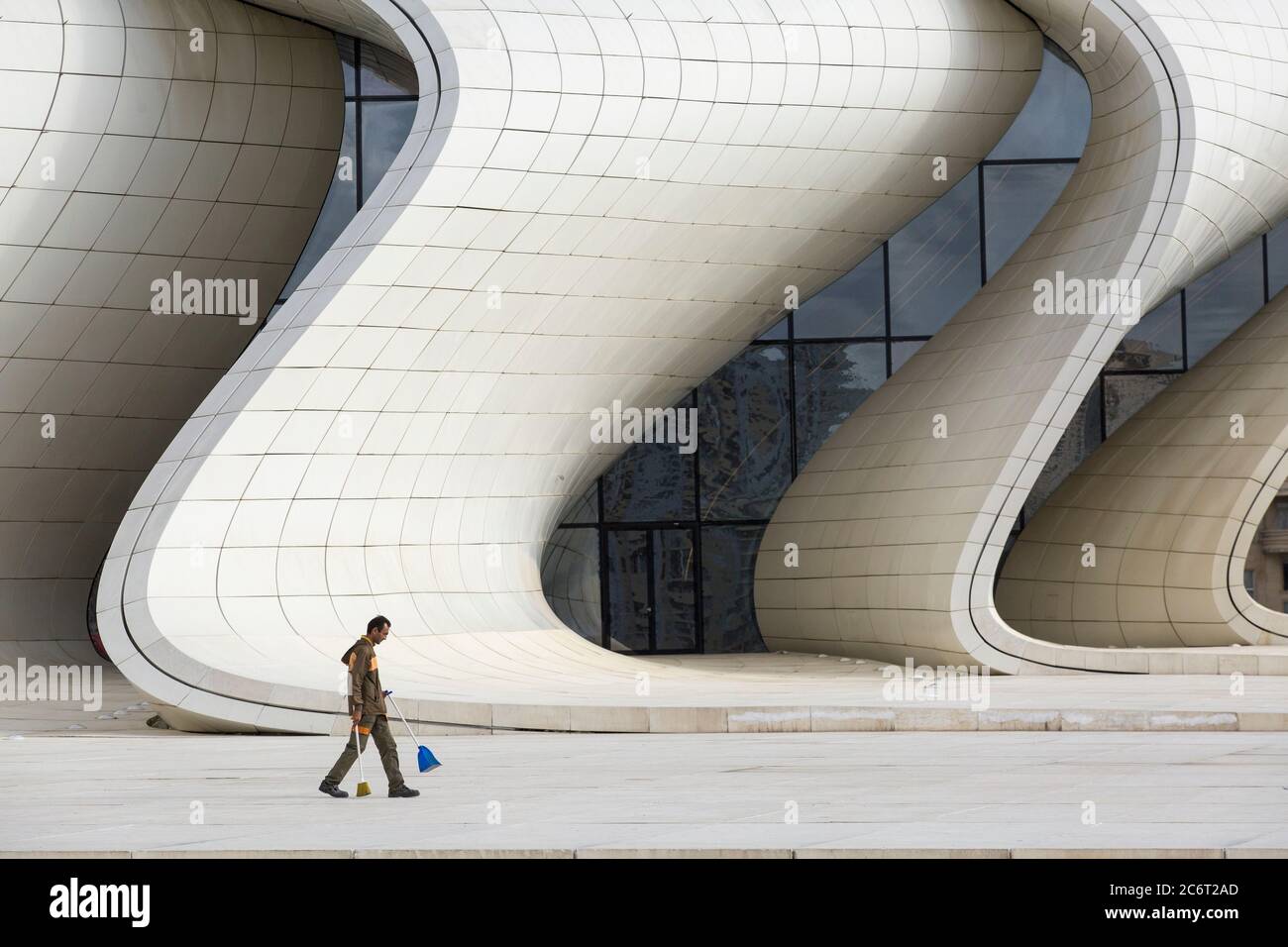 Un pulitore della città spazza su la lettiera davanti al centro di Heydar Aliyev progettato da Zaha Hadid il pezzo centrale dell'architettura moderna in Baku Azerbaigian Foto Stock