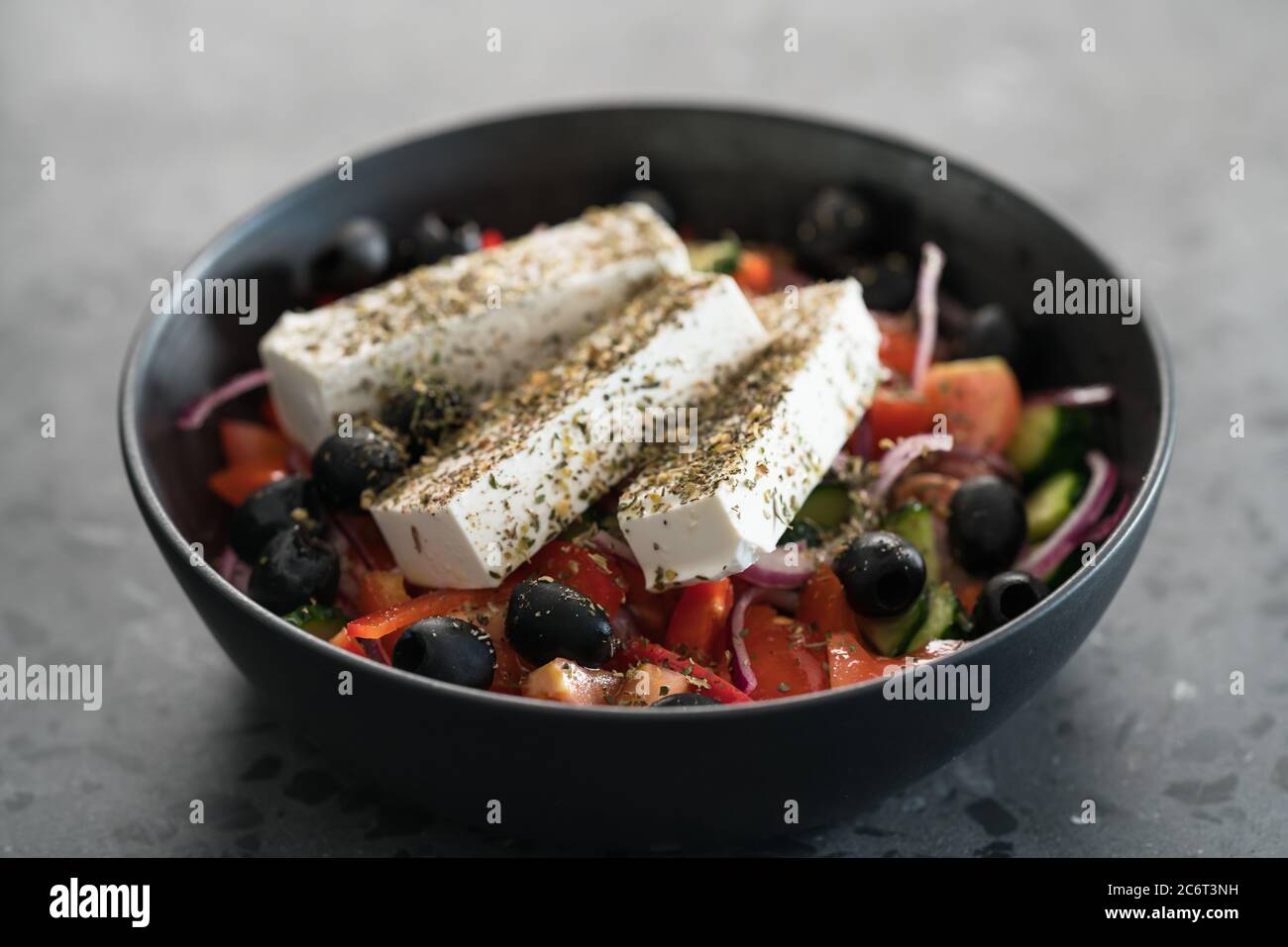 Insalata greca classica in ciotola nera su fondo di cemento Foto Stock