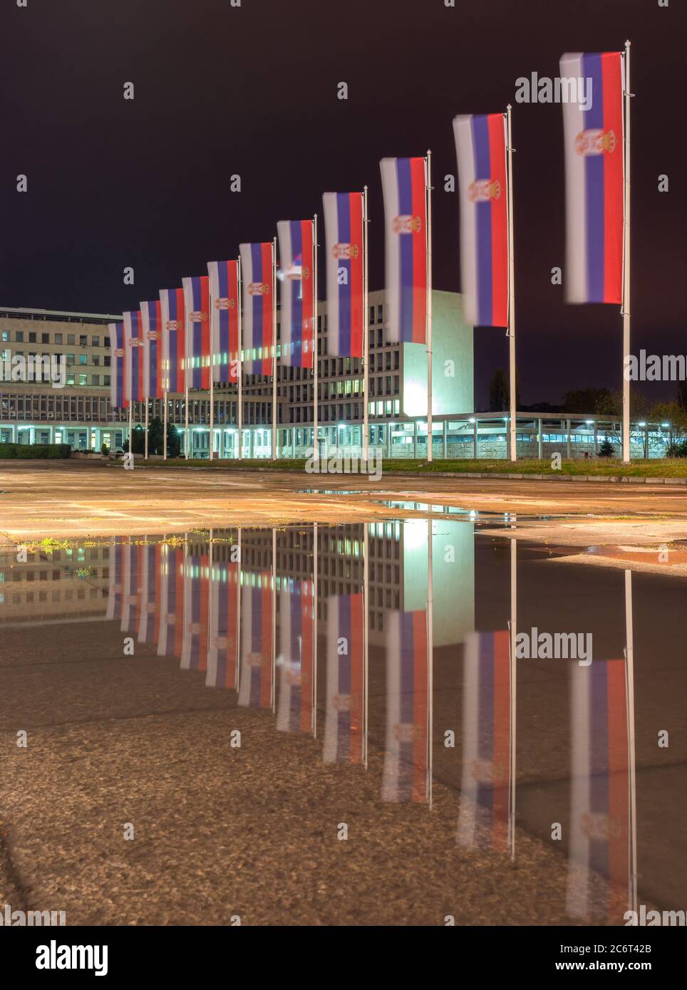 Bandiere della Serbia che si riflettono nel pozze d'acqua di notte, di fronte al palazzo della Serbia, sede di diversi ministeri del governo di Foto Stock