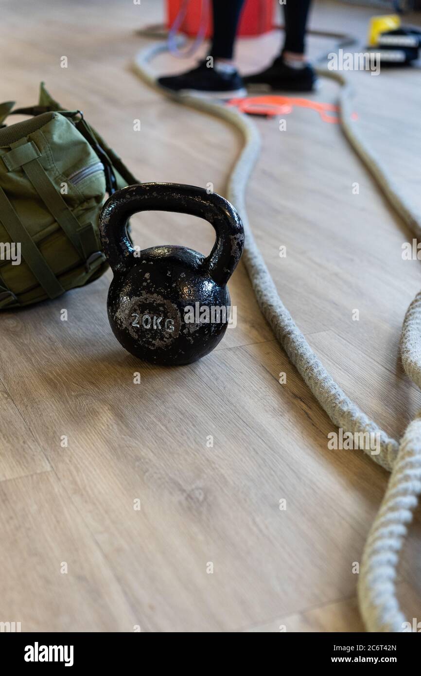 Attrezzature da palestra per il campo di stivali e allenati con il bicchiere del bollitore, la corda, la borsa da sabbia nella palestra sul pavimento. Gambe dell'istruttore sullo sfondo. Shot verticale. Foto Stock