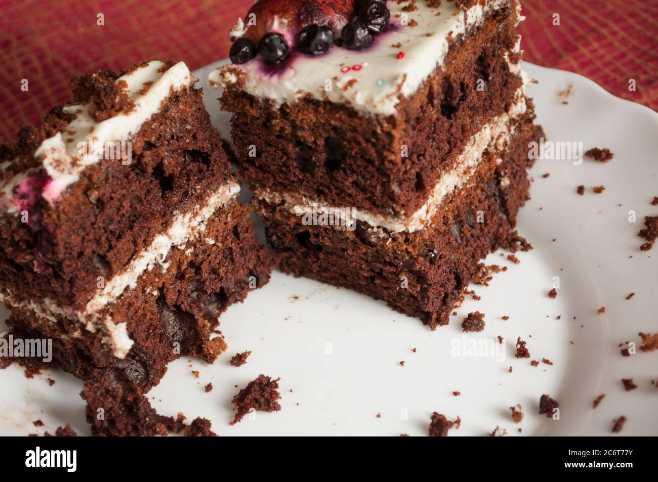 Gli ultimi due pezzi di pan di Spagna al cioccolato con panna su un piatto bianco sono decorati con una colorazione multicolore con briciole su un piatto da vicino Foto Stock