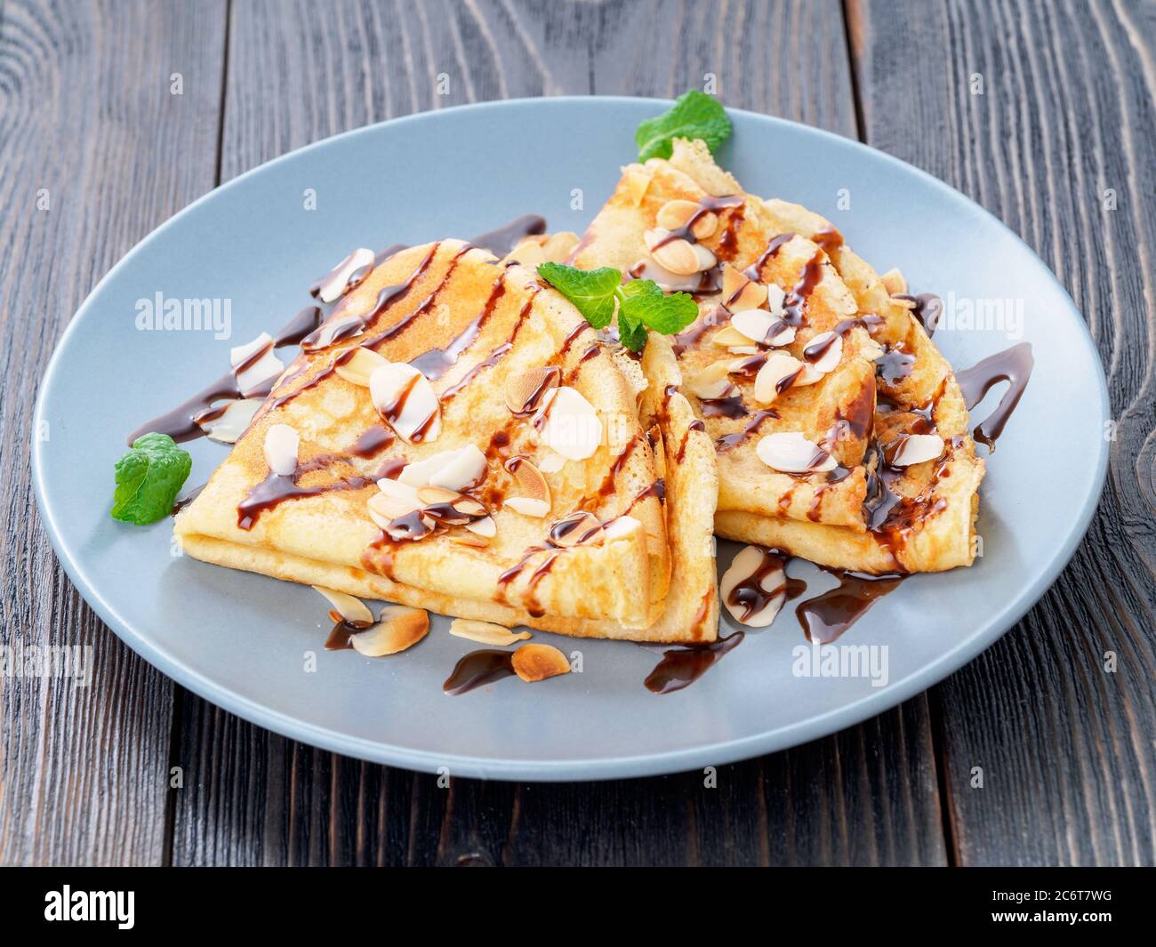 Due pancake con sciroppo di cioccolato, scaglie di mandorle su piatto, miele scorre dal cucchiaio, vista laterale Foto Stock