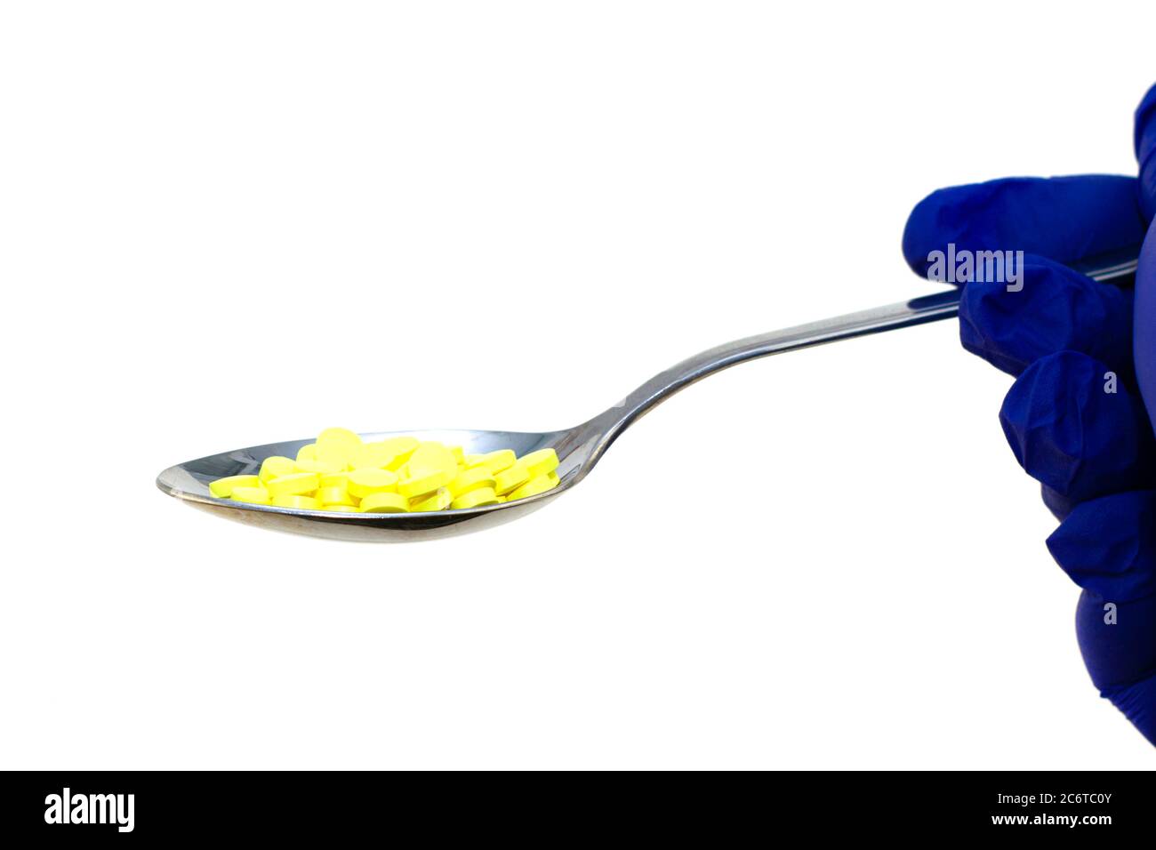 mano in un guanto chirurgico protettivo blu tiene un cucchiaio di ferro con pillole gialle su uno sfondo bianco Foto Stock