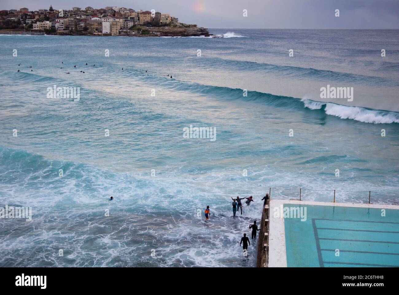 Nuotatori i surfisti in mute giocano a onde presso la piscina oceanica della spiaggia di Bondi Foto Stock