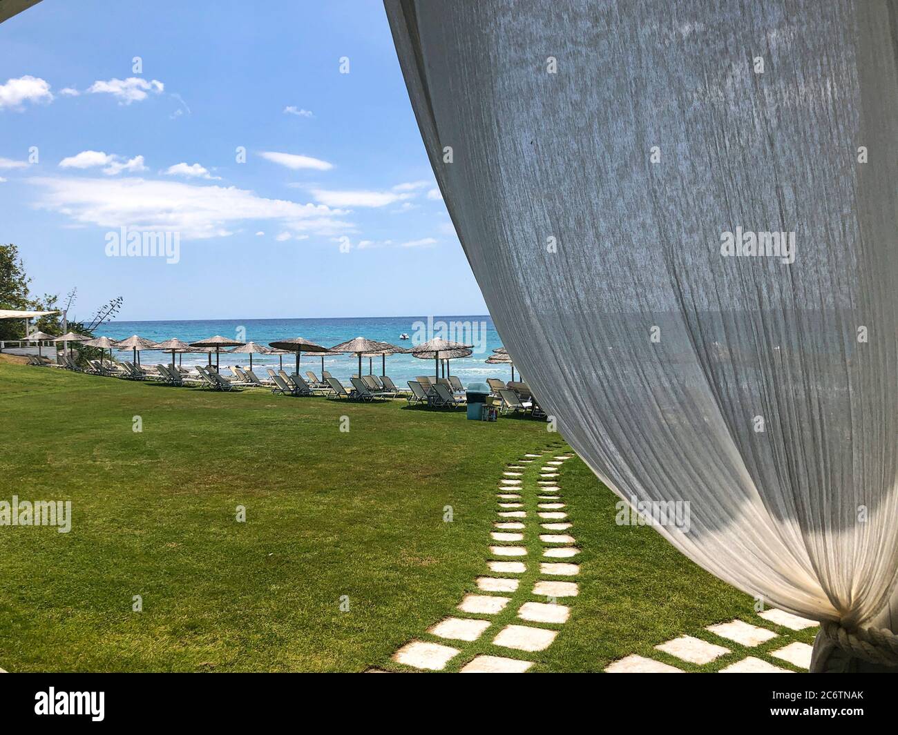 Panno bianco e un sentiero in pietra che conduce sulla spiaggia di fronte al mare con lettini e ombrelloni Foto Stock