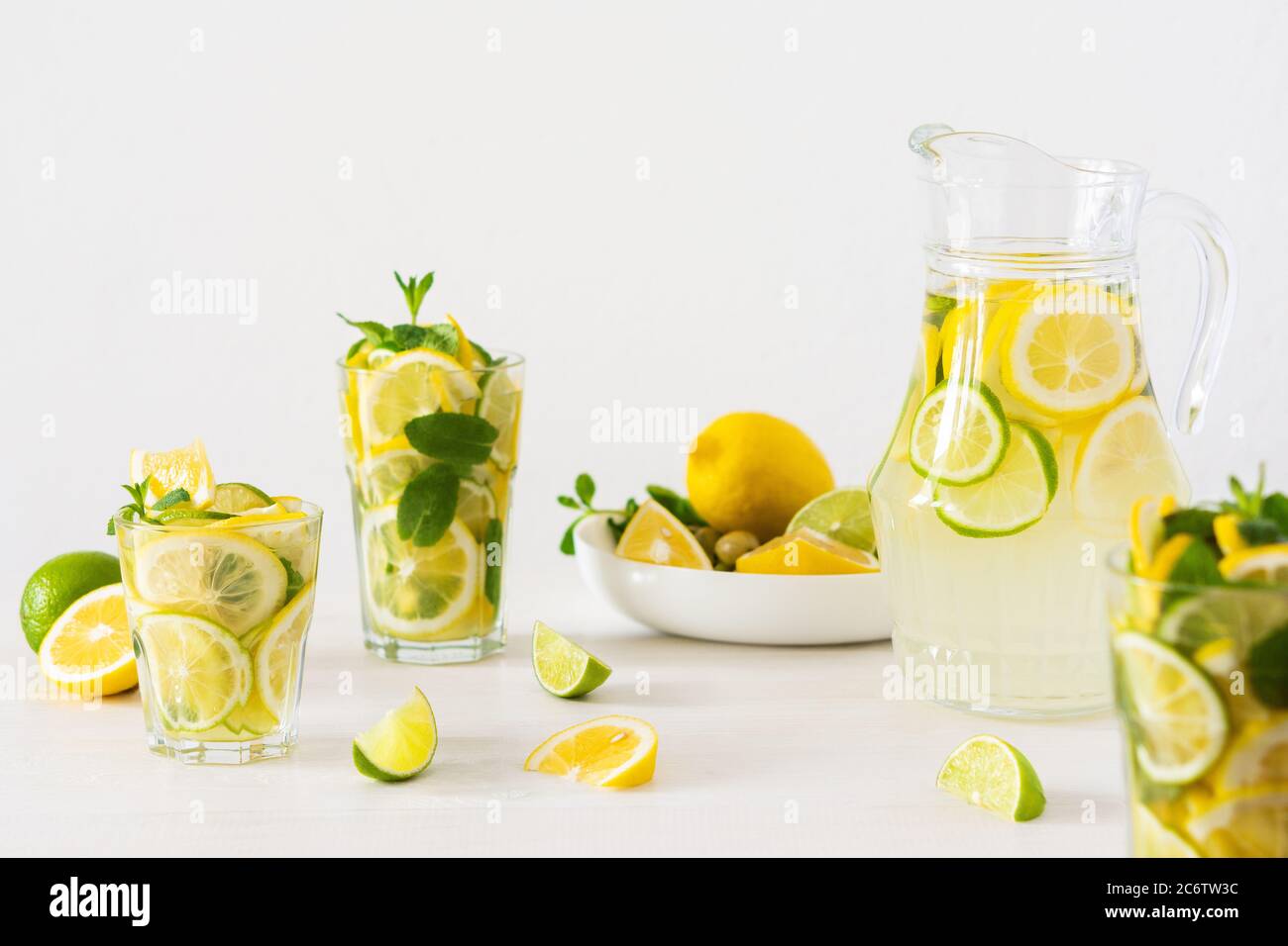 Bevanda estiva rinfrescante di limone, lime e menta, caraffa con limonata e bicchieri e fette di agrumi Foto Stock