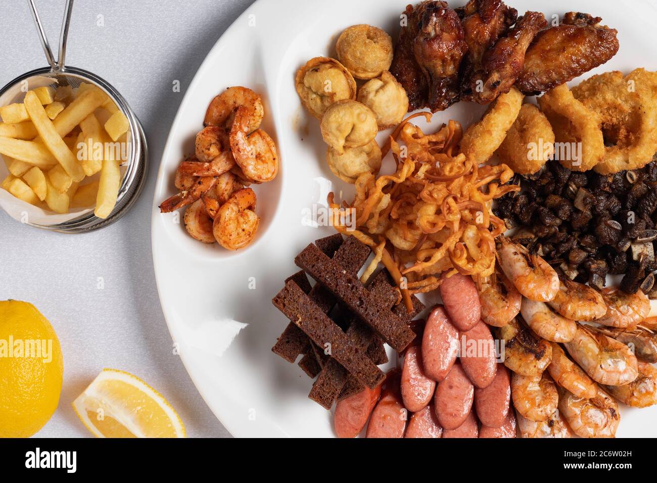 anelli di cipolla fritti, calamari impanati, patate croccanti, limone e salsicce alla griglia Foto Stock