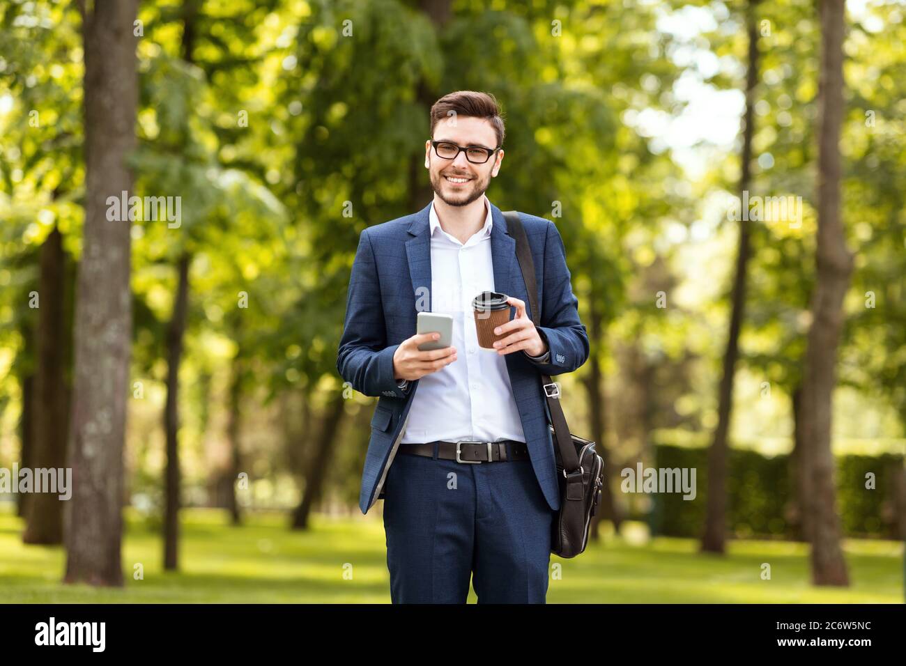 Buon lavoratore d'ufficio con il suo caffè mattina controllare le e-mail al telefono al parco il giorno di sole Foto Stock