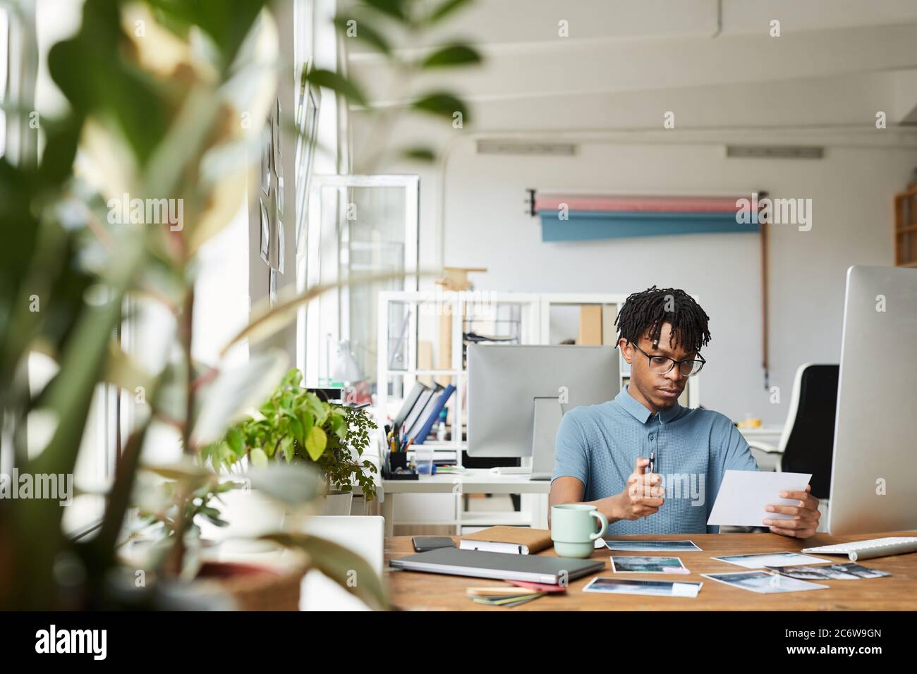 Ritratto di creativo afroamericano uomo revisione di fotografie mentre lavorando su editing e pubblicazione in ufficio moderno, copia spazio Foto Stock