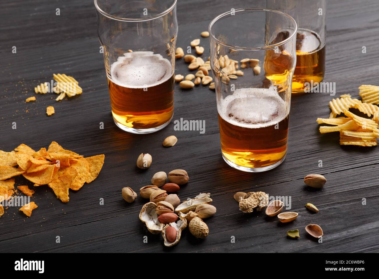 Birra alla spina. Bicchiere di birra e bottiglia incompiuta con bevanda, intorno sono arachidi, patatine e nachos Foto Stock