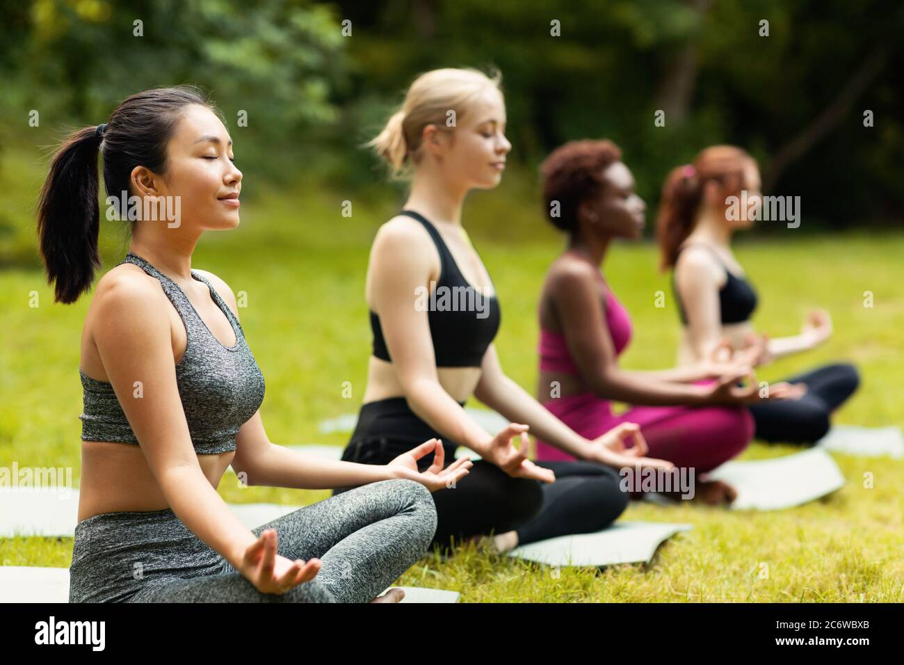 Concentrate multinazionali Signore meditare o fare esercizi di respirazione sulla pratica yoga fuori, spazio vuoto Foto Stock