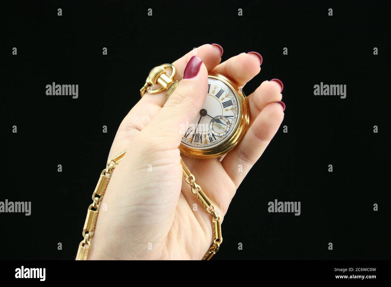 Sfondo nero di una mano femminile giovane che tiene in mano l'orologio da tasca d'oro con catena. Foto Stock