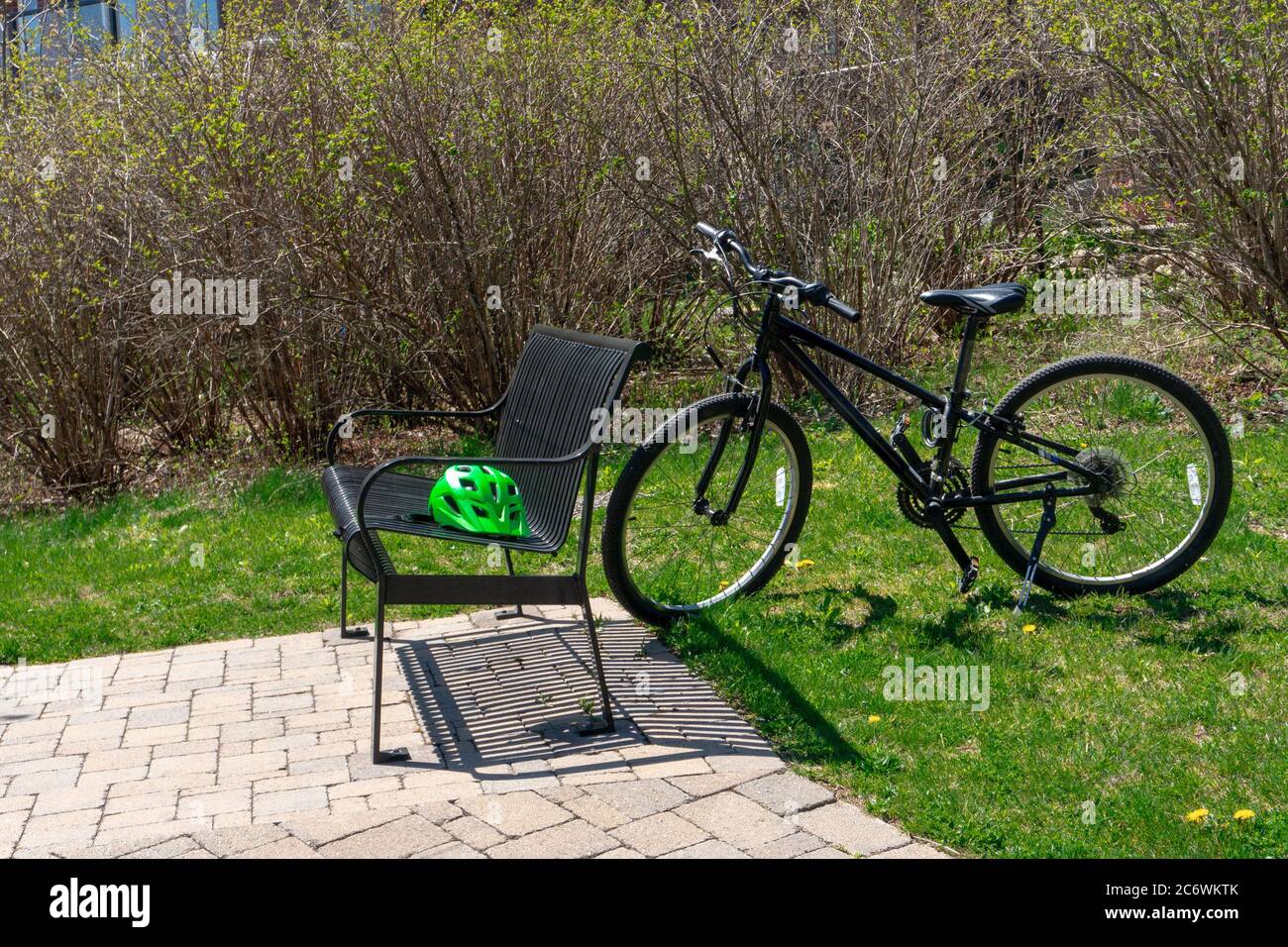 Una bicicletta è in piedi sull'erba, vicino ai cespugli, e accanto ad essa su una panchina di giardino in metallo è un casco verde Foto Stock