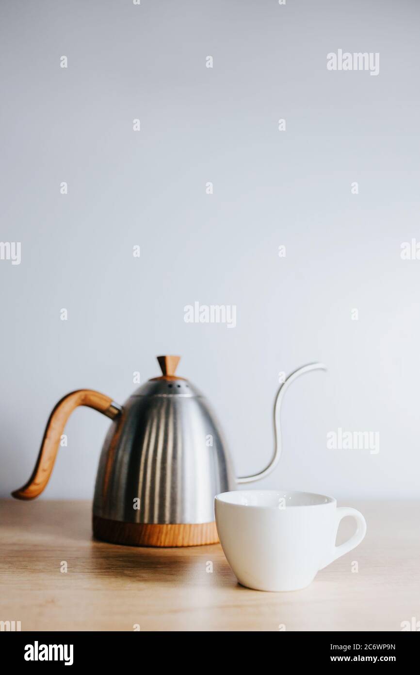 Elegante bollitore in acciaio inossidabile con naso lungo e ricurvo e una  tazza in ceramica bianca sul tavolo per preparare tè o caffè con metodo  antigoccia Foto stock - Alamy