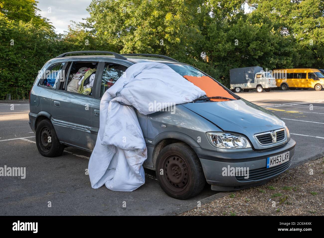 Un'auto abitata da una persona senza casa, piena di vestiti e oggetti personali, con il parabrezza anteriore coperto, Regno Unito Foto Stock