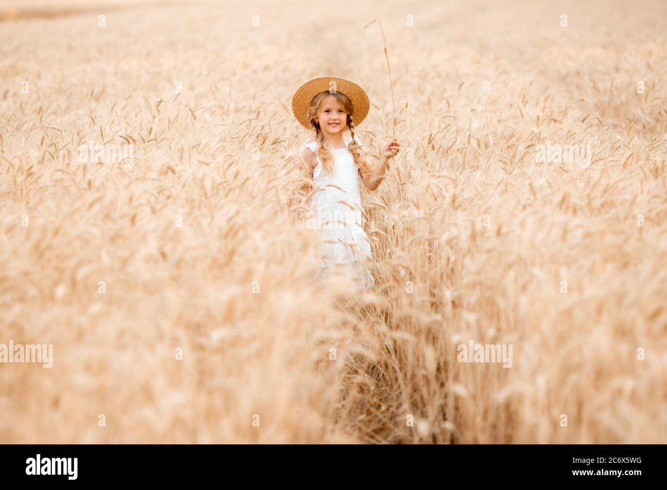Adorabile bambina gioca su un campo di grano in una calda giornata estiva Foto Stock