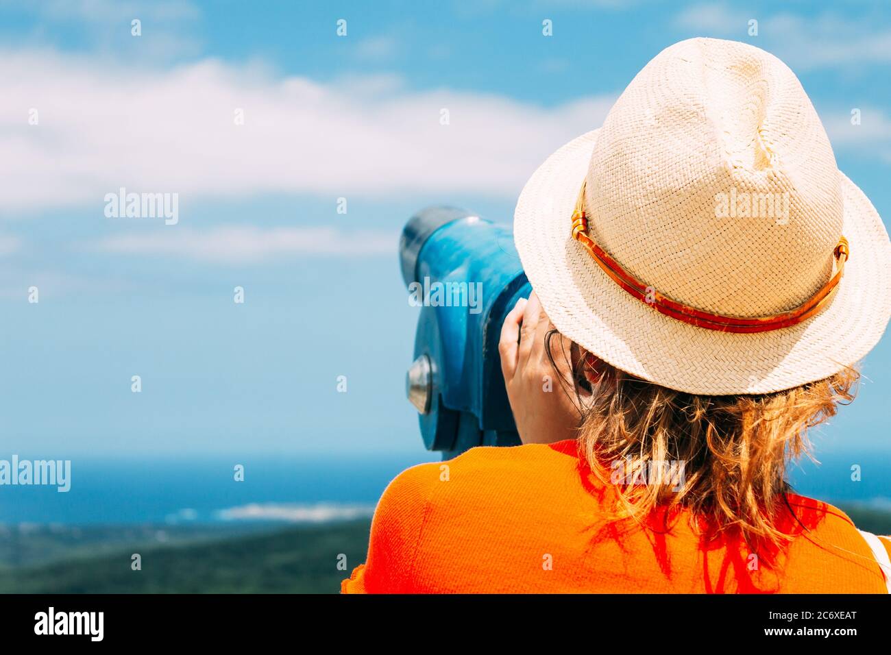 Una ragazza in un cappello di paglia guarda attraverso il binocolo della città. Concetto di viaggio. Foto Stock