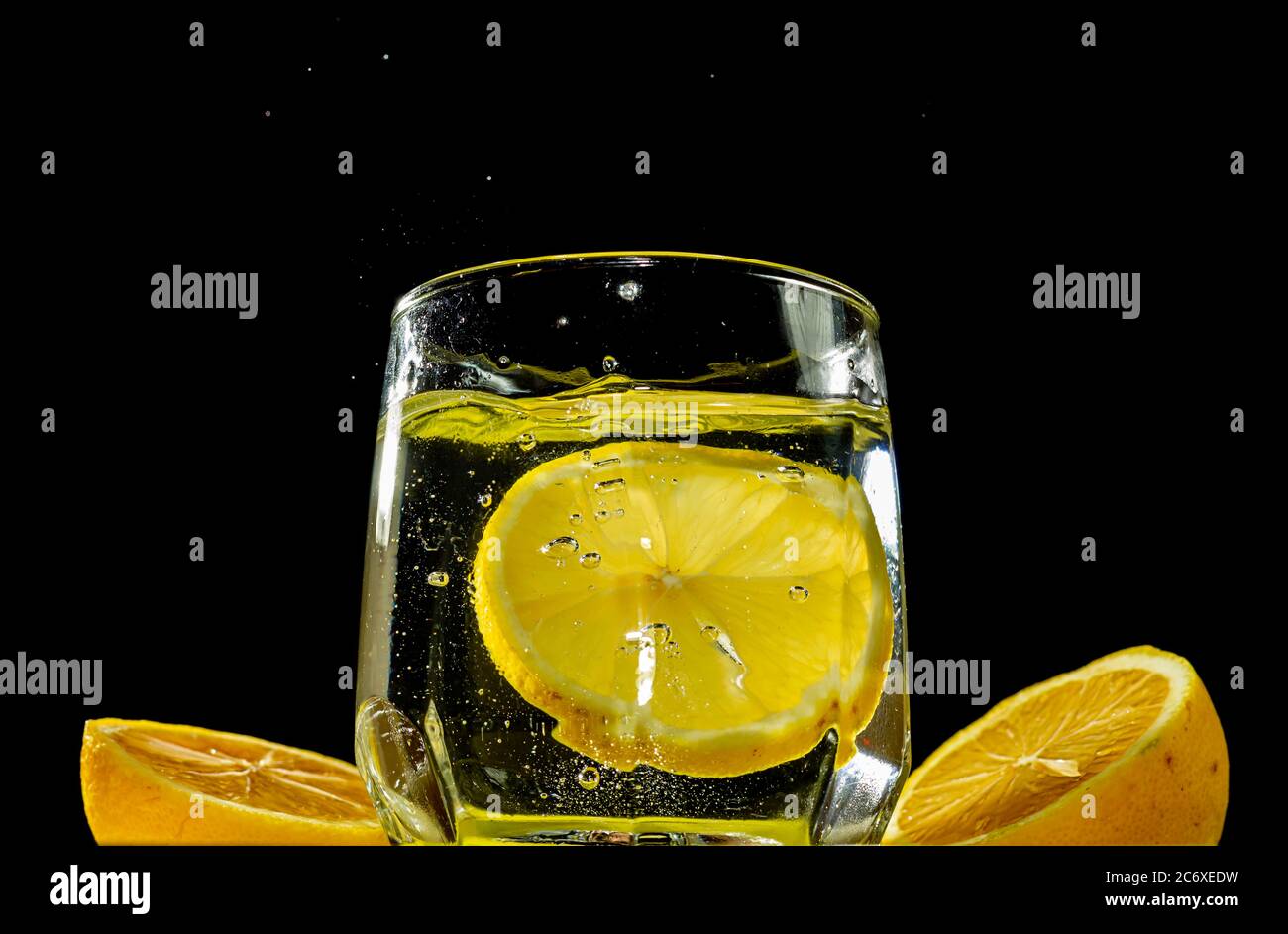 Per bere, una fetta di limone viene gettata in un bicchiere di soda in estate. Gocce d'acqua che fuoriescono dalla soda davanti allo sfondo nero Foto Stock