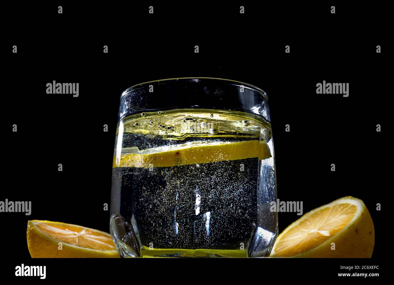 Per bere, una fetta di limone viene gettata in un bicchiere di soda in estate. Gocce d'acqua che fuoriescono dalla soda davanti allo sfondo nero Foto Stock