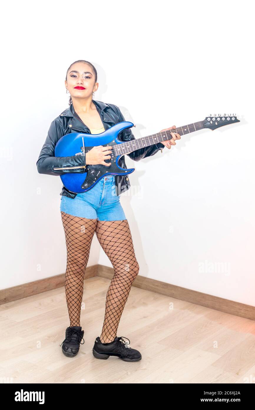 Teen girl che suona la chitarra elettrica in vestito nero e oro rock. Attività a casa durante la quarantena Foto Stock