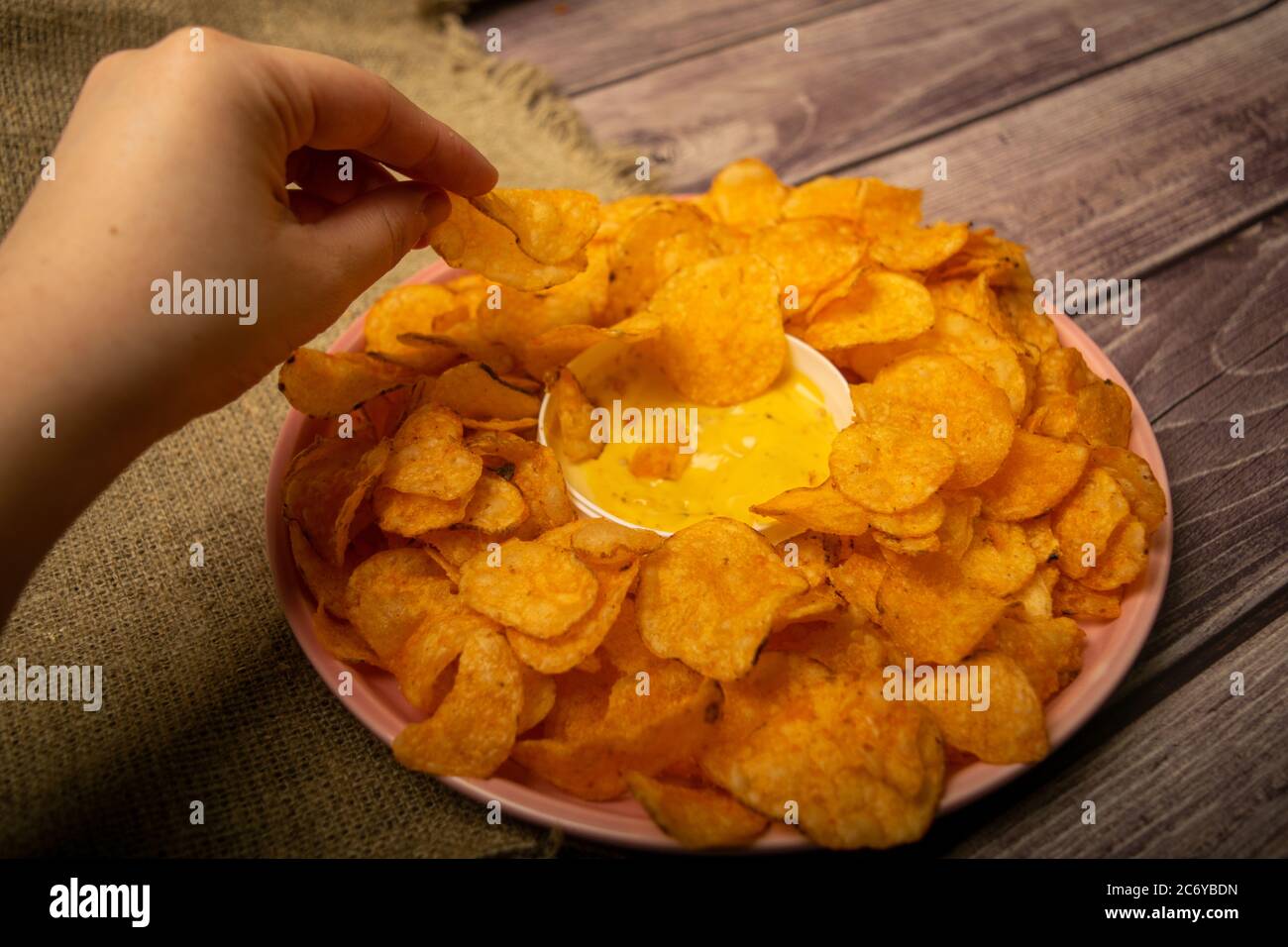 La ragazza prende un chip da un piatto rotondo con patatine e una pentola con salsa di formaggio al centro del piatto. Primo piano Foto Stock