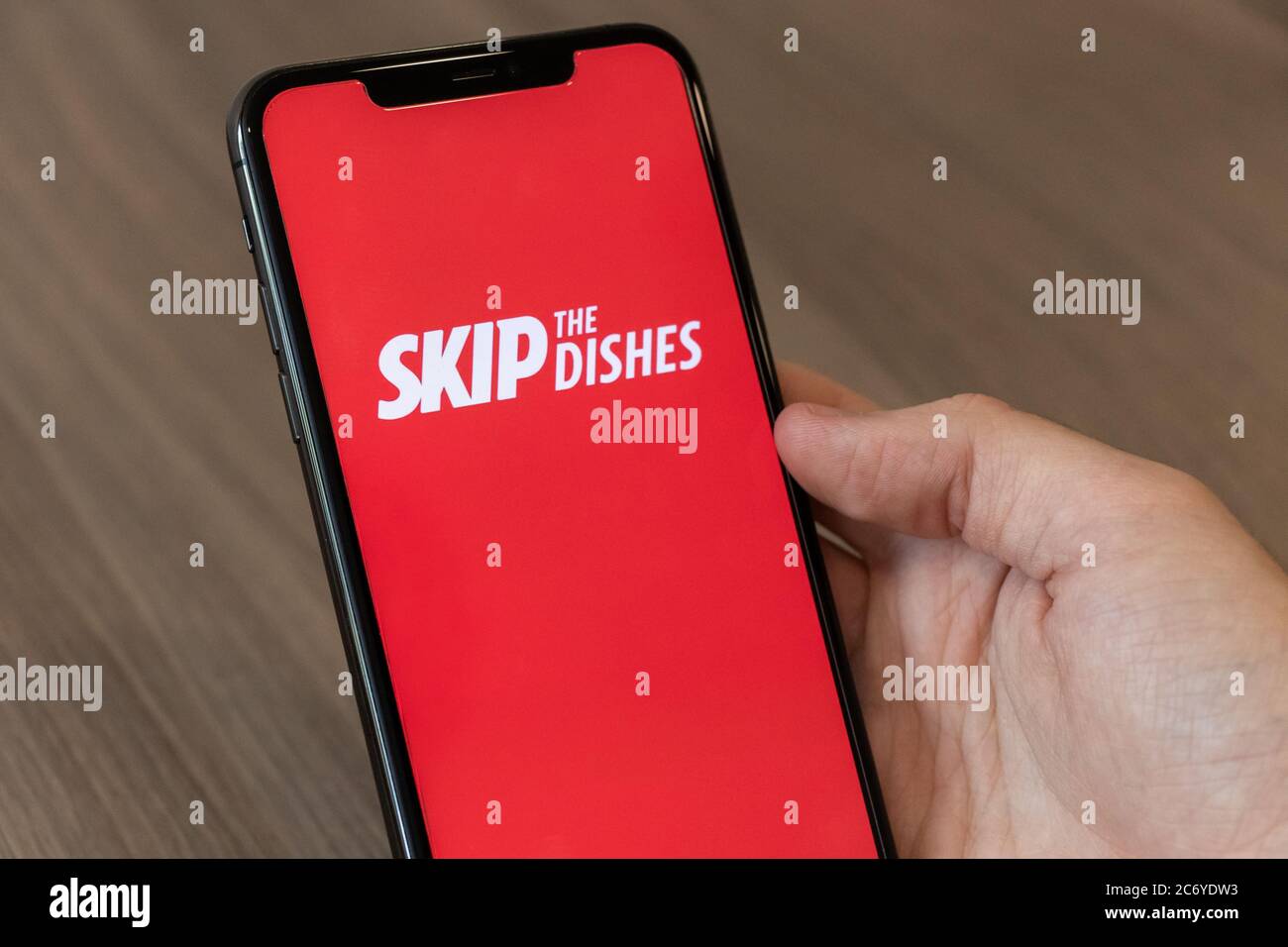 Persona che usa un cellulare con il logo Skip the Dishes, il popolare servizio online di ordinazione e consegna di cibo su schermo. Foto Stock