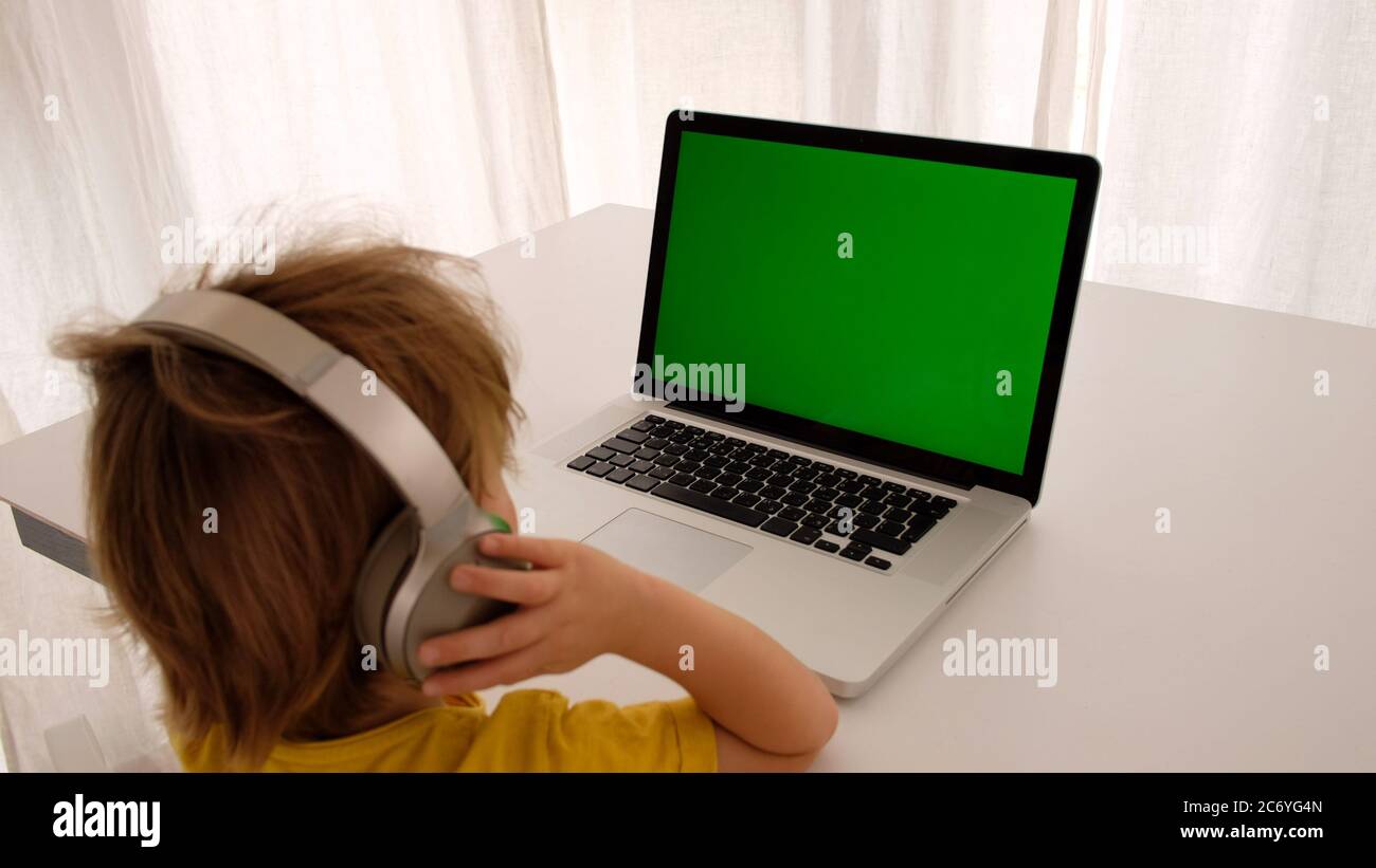 Bambino in cuffia davanti allo schermo verde del computer portatile Foto Stock