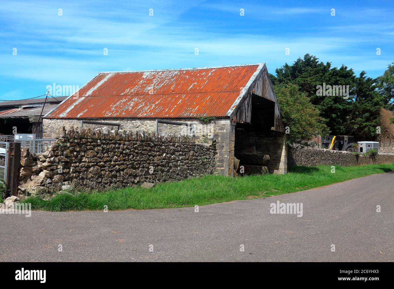 Un vecchio negozio sul lato della strada per attrezzi agricoli o trattori molto grandi o persino una mietitrebbia, con un tetto in stagno arrugginito e un ingresso a pianta aperta. Foto Stock
